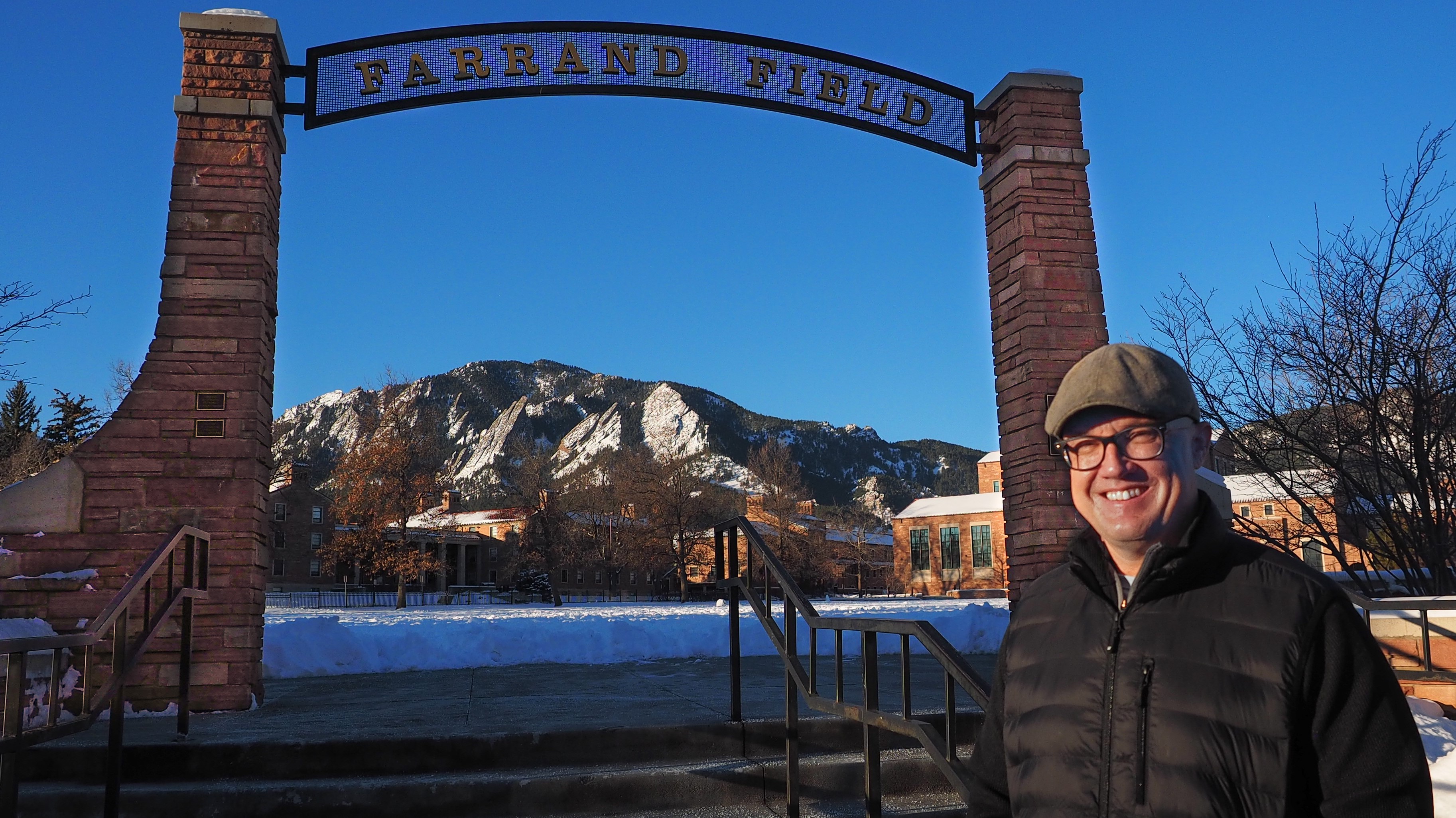 Photo of Kelsey Draper, a senior HR professional with Infrastructure and Sustainability, stands in front of the archway to Farrand Field on the CU Boulder campus. He's standing in the right foreground.
