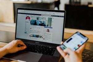 Person using mobile device and laptop simultaneously to access social media.