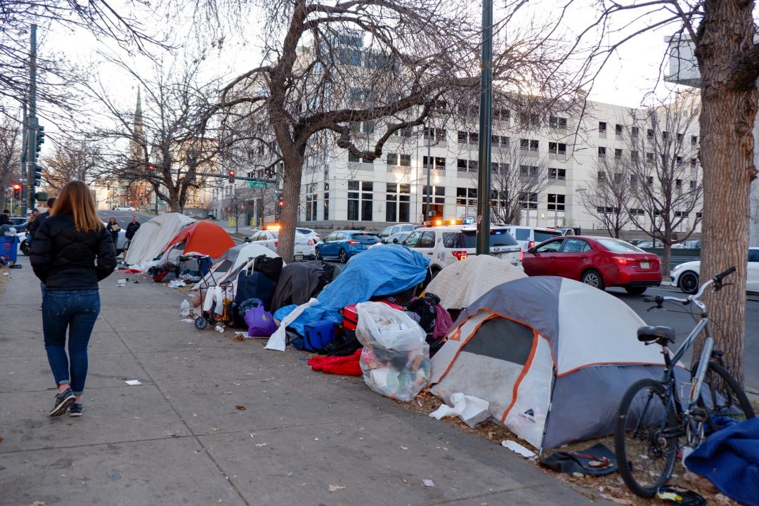 Photo of tents along a Denver sidewalk with a person walking by, facing away form the camera, on the left side of the frame.
