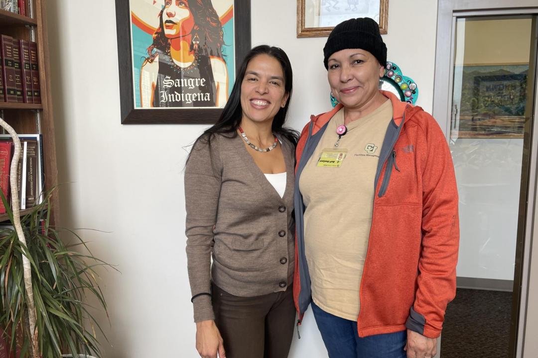 Violeta Chapin standing with Irma Bernard, a woman the clinic helped become a U.S. citizen. Chapin wearing a brown cardigan and pants. Bernard wearing a tan CU shirt and orange jacket. 