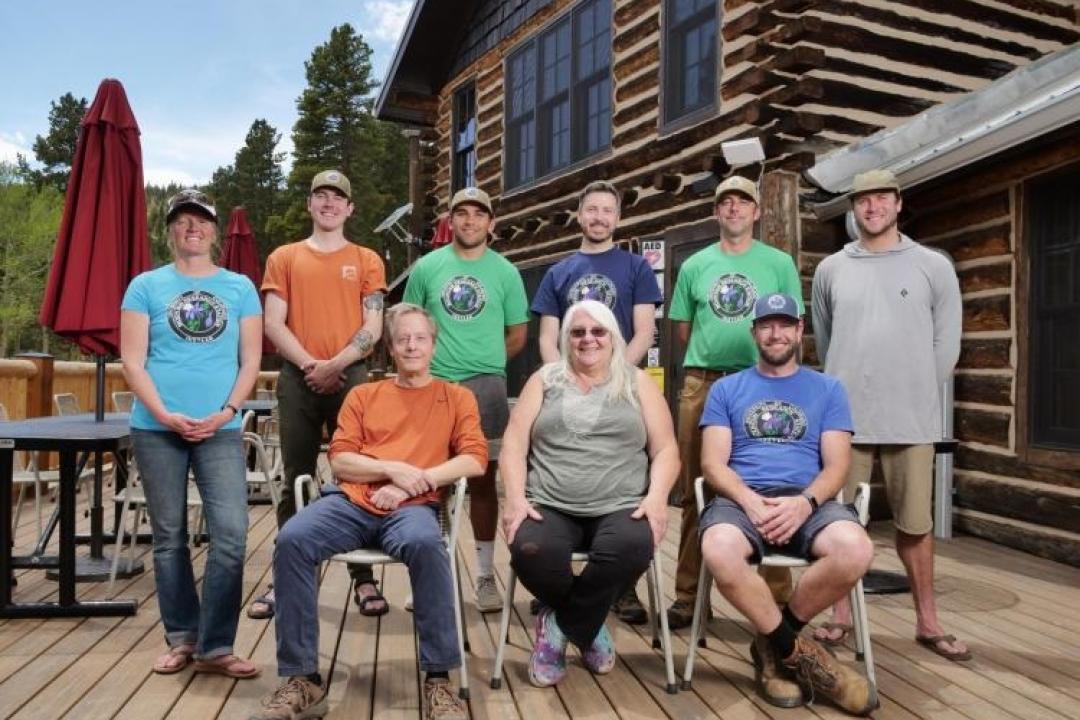 Mountain Research Center group photo outside on wood deck with wood cabin behind. 9 total members. 
