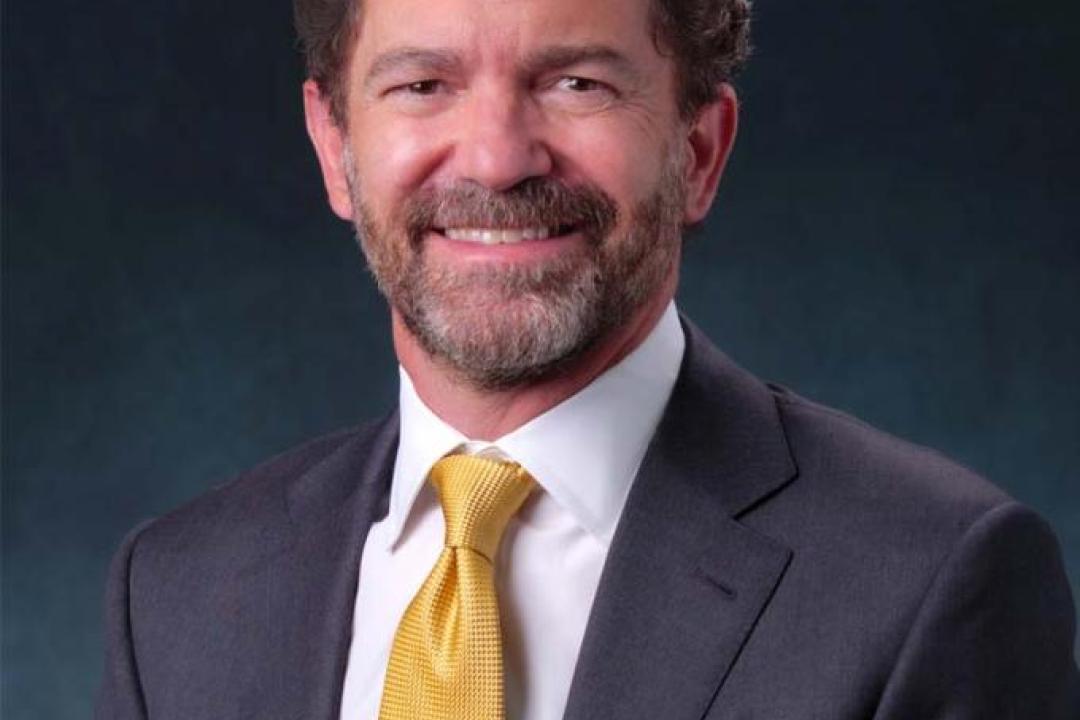 CU President Todd Saliman sitting with a dark suit and yellow tie, smiling