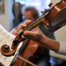 Photo of two hands playing a violin over a music stand with sheet music.