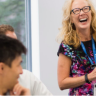 Photo of Dr. Tina Brock standing in a classroom and laughing as people seated in the left foreground look on.