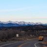 Photo of bus driving along a rural road with mountains in the background.