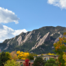 Photo of the Boulder Flatirons rising above trees with autumn leaves in the foreground.