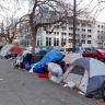 Photo of tents along a Denver sidewalk with a person walking by, facing away form the camera, on the left side of the frame.