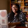 Photo of Shamika Klassen seated at a table with her laptop facing the camera.