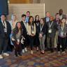 group photo of students and faculty. Blue, brown, and tan designed floor with beige wall