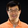 Dr. Jun Ye smiling for a portrait photo with an orange polo