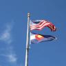 Photo taken form low angle of the U.S. and Colorado state flags on a flagpole against a blue sky.
