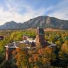 Aerial photo of CU Boulder's Old Main building surrounded by autumn foliage with the Flatirons rock formations visible in the background.