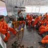 Photo of one instructor and a couple dozen students, all in bright orange environment suits, gathered in a building for a presentation during a simulation exercise at the Mars Desert Research Station in 2019.