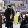 picture of an outdoor cu denver graduation ceremony. A speaker is pictured with his back to the camera speaking to the crowd in a black graduation robe. 