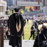 picture of an outdoor cu denver graduation ceremony. A speaker is pictured with his back to the camera speaking to the crowd in a black graduation robe. 