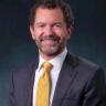 CU President Todd Saliman sitting with a dark suit and yellow tie, smiling