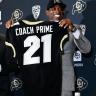 Coach Deion Sanders holding a black CU jersey with Coach Prime on the back 